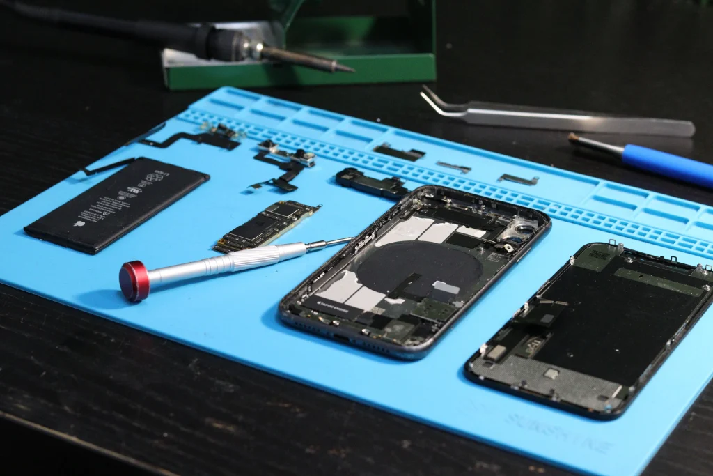 iPhone despiezado sobre tapete de reparación con batería, placa y destornillador de precisión